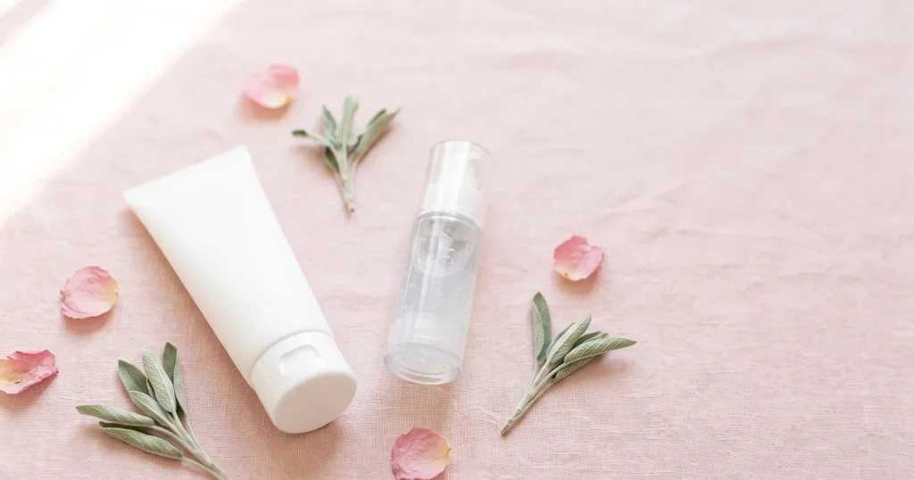 Azelaic acid before and after guide with a white cream tube and clear gel pump on blush pink beside rose petals and sage sprigs
